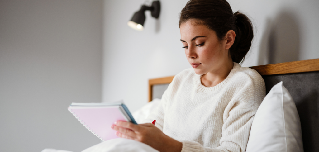 A woman writing down notes while sitting in bed at home.