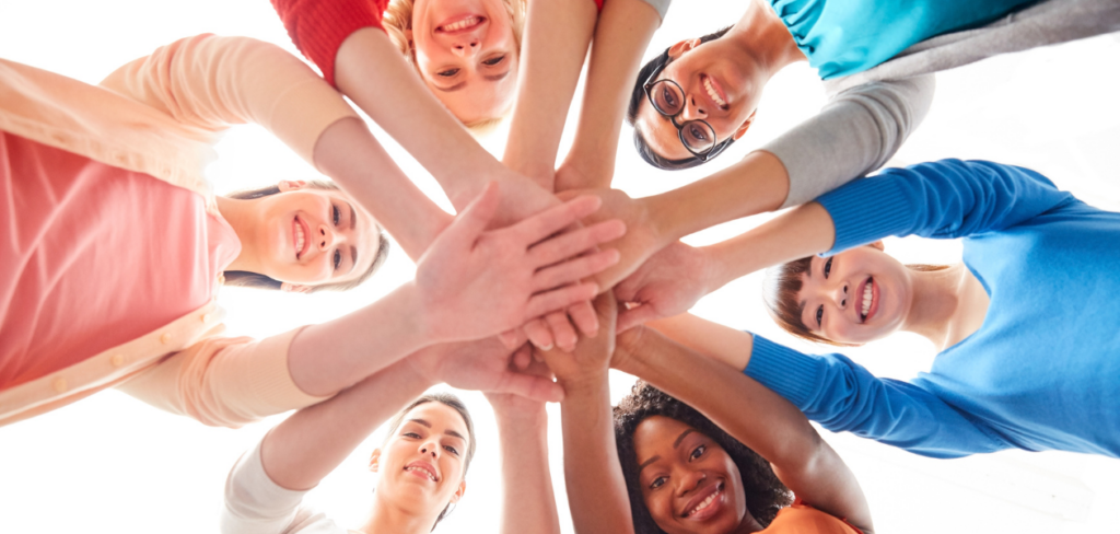 A group of women in a circle with their hands on top of each other.
