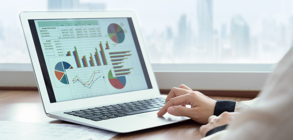 A close-up picture of a person using a laptop while looking at charts and graphs.


