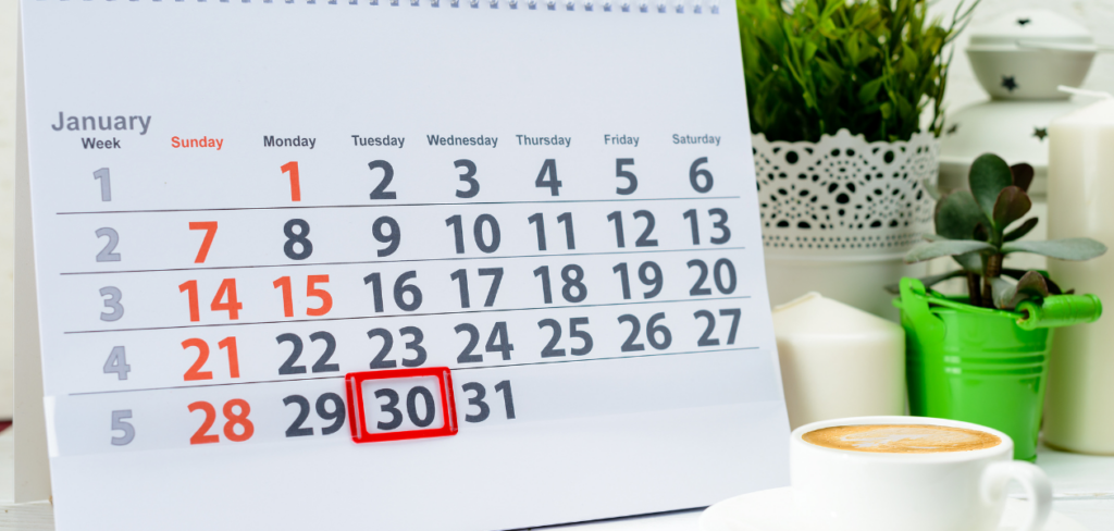 A shot of a calendar displaying Day 30 of the month on a white background, accompanied by coffee and plants.