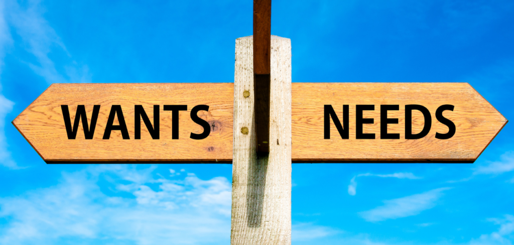 A wooden signpost with two opposite arrows against a clear blue sky, with the words "wants" and "needs" on it.