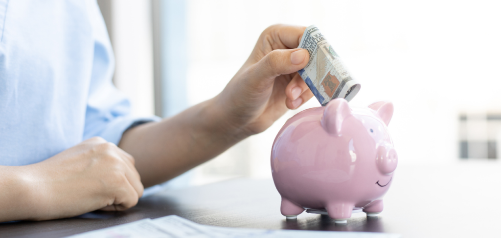 A hand putting money into a piggy bank for saving.

