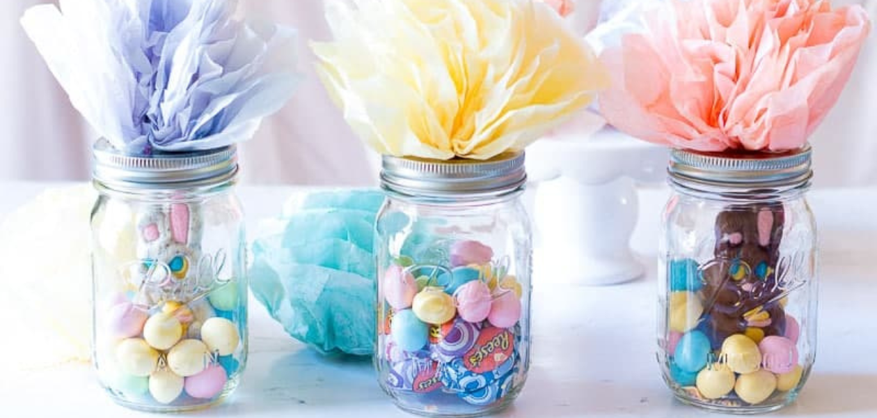 Three glass jars filled with candies and chocolates, topped with pastel-colored paper decorations.