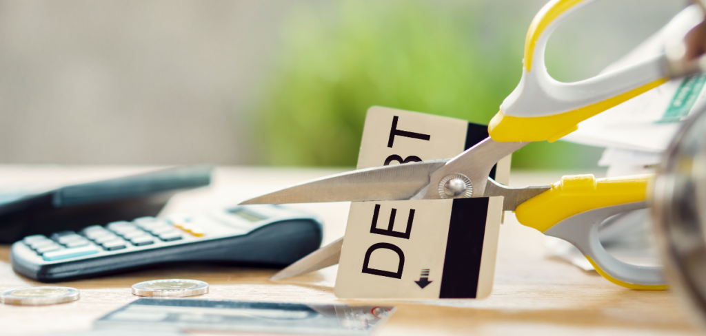 A debt-free concept is depicted with scissors cutting a credit card, alongside a calculator and bills on a desk.