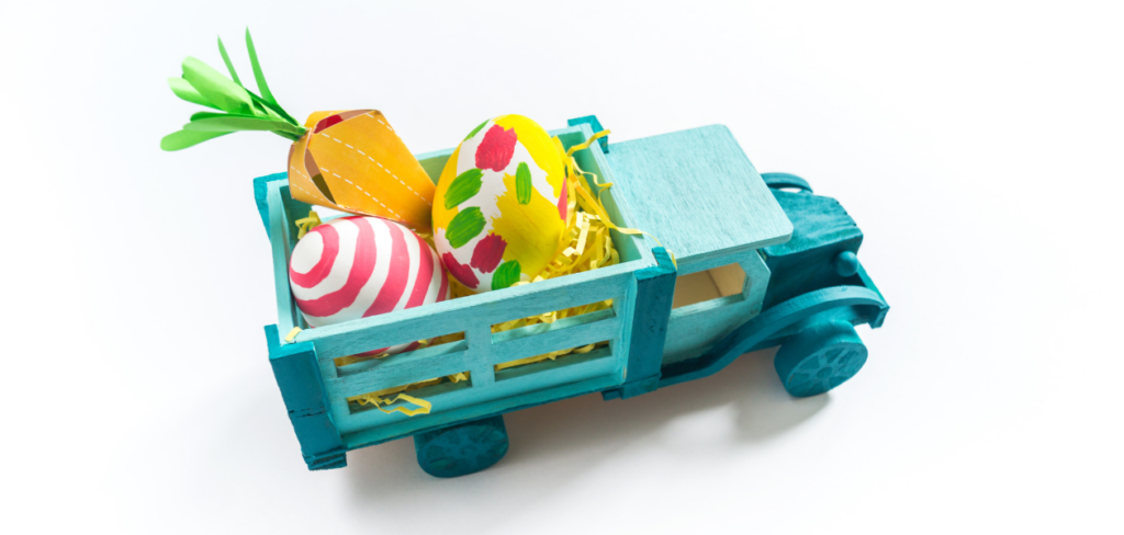 A paper carrot gift bag and Easter eggs are inside a blue wooden toy truck.
