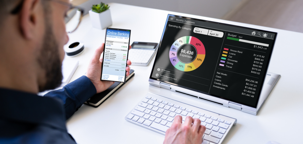 A man is looking at a money planning budget tracker app on a phone and laptop.