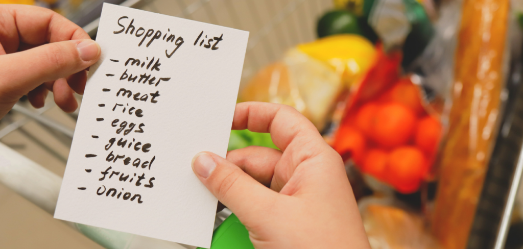 A woman holding a shopping list at the supermarket, pushing a grocery cart filled with products.


