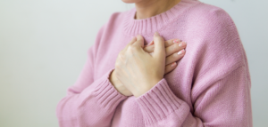Woman wearing a pink sweater holding her hands over her chest.