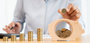 Person stacking coins and placing them in a wooden piggy bank.