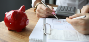 Two people reviewing a financial plan with the words 'Pay off Debts' highlighted, alongside a red piggy bank, calculator, and paperwork.