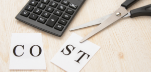Concept of cutting costs—calculator, scissors, and the word 'COST' cut in half.
