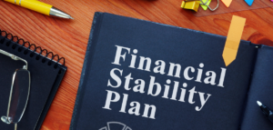 Notebook titled 'Financial Stability Plan' on a desk with glasses and pen.