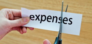 A close-up of hands cutting a piece of paper with the word 'expenses'.
