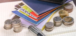 Stacks of coins, a pen, and several colorful passbooks arranged on a graph paper notebook.