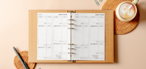 A flatlay image of a budgeting journal on a beige surface. A cup of coffee and paper clips are also visible.
