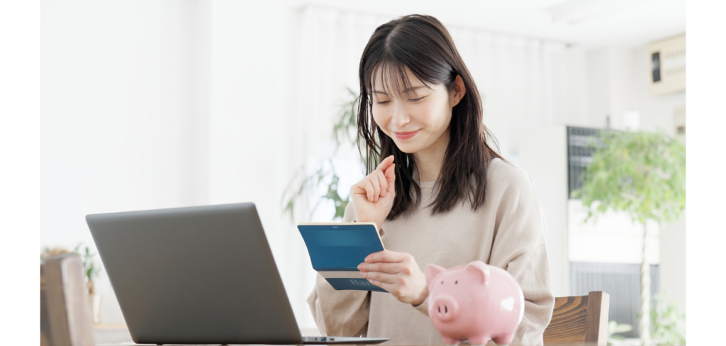 A young woman smiles as she reviews her bank statement at her laptop, with a piggy bank beside her.