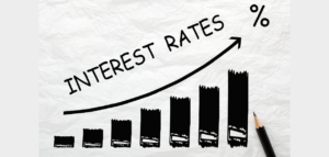 A hand-drawn graph on crumpled paper shows interest rates rising sharply, indicated by an upward-trending line and increasing bar heights. A pencil rests beside the drawing.