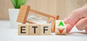 Wooden blocks spelling "ETF" are next to an hourglass and a block with a green and red arrow.
