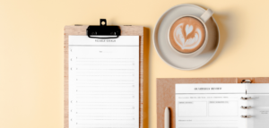 The image shows a clipboard with a "Yearly Goals" sheet, a planner with a "Quarterly Review" page, and a cup of coffee.
