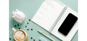 Budget review notebook, smartphone,  coffee, and piggy bank on a mint green background.