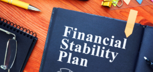 Open book with the title "Financial Stability Plan" on a wood desk with office supplies.