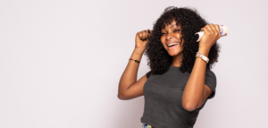 A young woman joyfully holds up a roll of cash, celebrating a financial success. She is smiling broadly and has her fists raised in the air.