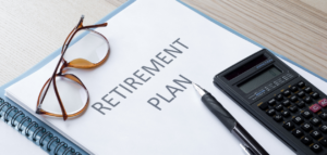 A retirement plan document lies open on a desk, accompanied by a calculator, pen, and eyeglasses.