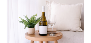 A bottle of white wine sits on a small wooden side table next to an empty wine glass and a small potted fern.
