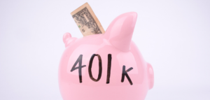 A pink piggy bank with "401k" written on it has a one dollar bill inserted into its slot.