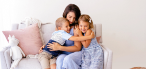 A mother embracing her two young children, a boy and a girl, who are hugging her tightly. 