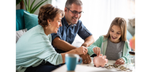 A family, a grandmother, father, and daughter, smiles as they add coins to a piggy bank together.