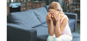 A woman sits on a couch, head in her hands, appearing upset or stressed.