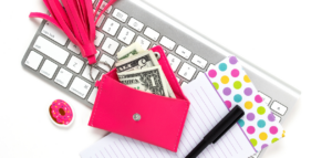 A flat lay image showing a keyboard, a small pink wallet with cash inside, a black pen, and two colorful notebooks.