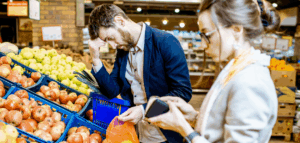 A man and woman standing in a grocery store, looking stressed while checking their wallets.