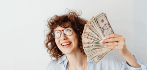 Smiling woman holding up a fan of US dollar bills.
