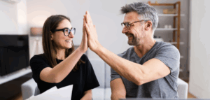 Man and woman smiling and giving each other a high-five, with papers on the table in front of them.