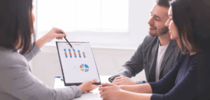 Financial advisor presenting bar and pie charts to a young couple, explaining financial data or investment options as they listen attentively.